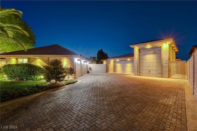 property exterior at night featuring decorative driveway, fence, a gate, and stucco siding