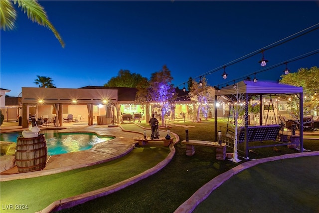 pool at night with a patio and a lawn