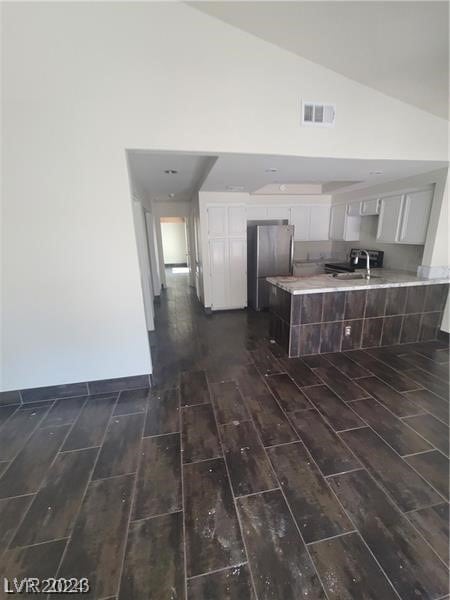 kitchen with dark hardwood / wood-style floors, stainless steel fridge, white cabinetry, and high vaulted ceiling