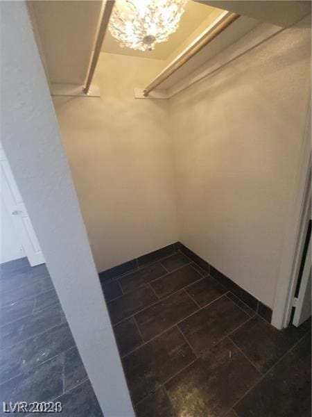 spacious closet with dark tile patterned floors and an inviting chandelier