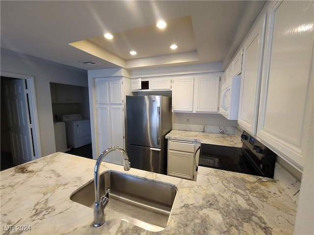 kitchen featuring sink, washer and dryer, stainless steel fridge, black / electric stove, and white cabinetry