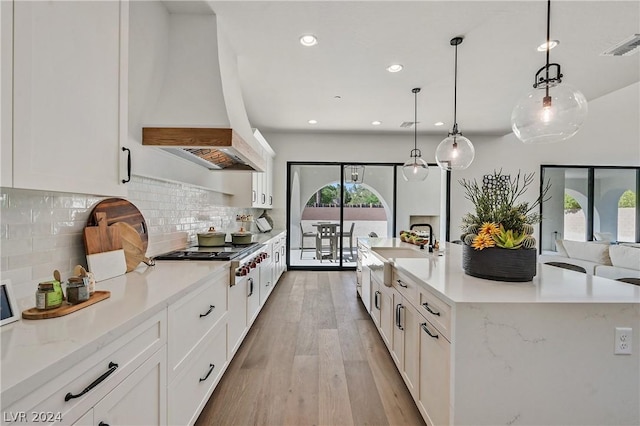 kitchen with stainless steel gas stovetop, white cabinetry, pendant lighting, and light hardwood / wood-style flooring