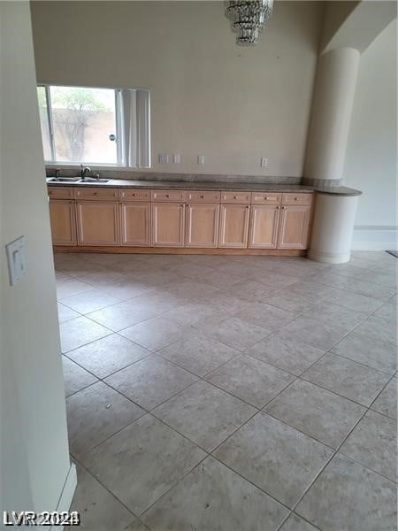 tiled empty room featuring sink, a chandelier, and a towering ceiling