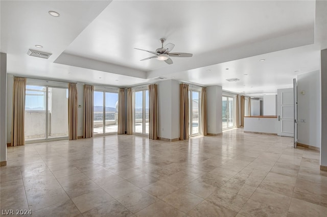 empty room with ceiling fan, a tray ceiling, and light tile floors