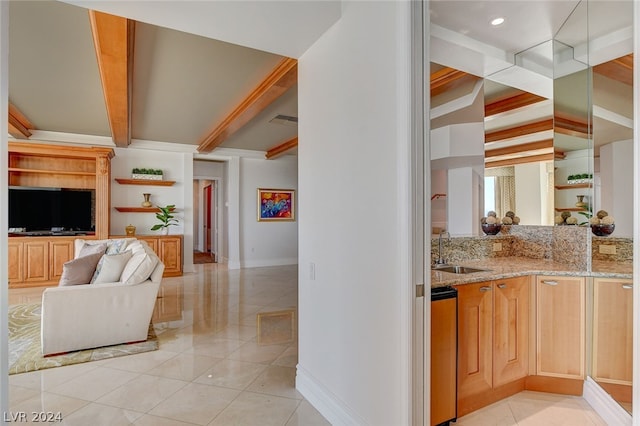 kitchen with light stone counters, beamed ceiling, ornamental molding, light tile floors, and sink