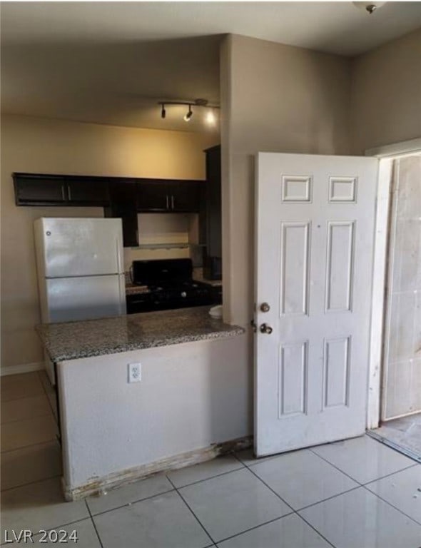 kitchen with range, light tile flooring, stone counters, white fridge, and track lighting