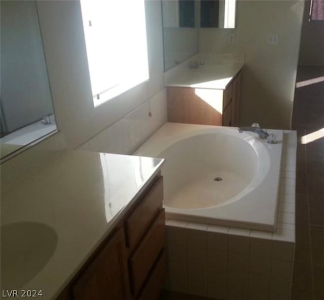 bathroom with vanity with extensive cabinet space, a relaxing tiled bath, and dual sinks