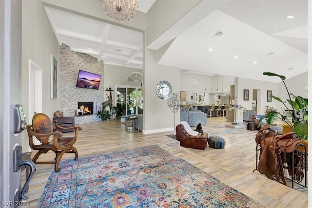 living room featuring a fireplace, light hardwood / wood-style floors, a chandelier, beam ceiling, and coffered ceiling