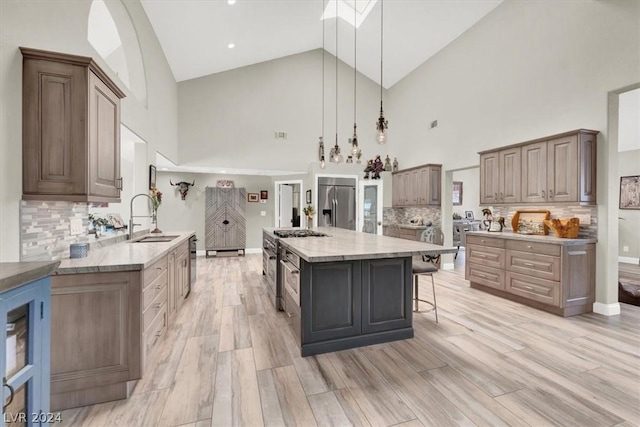 kitchen featuring pendant lighting, a kitchen island, sink, appliances with stainless steel finishes, and high vaulted ceiling