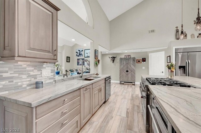 kitchen featuring appliances with stainless steel finishes, light brown cabinets, high vaulted ceiling, light stone counters, and sink