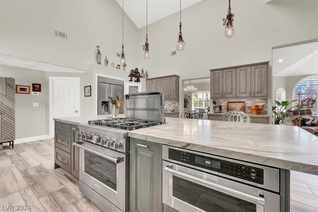 kitchen featuring light stone countertops, appliances with stainless steel finishes, hanging light fixtures, a large island, and high vaulted ceiling