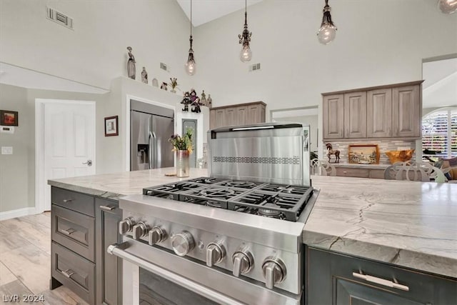 kitchen with light stone countertops, pendant lighting, stainless steel appliances, light hardwood / wood-style floors, and high vaulted ceiling