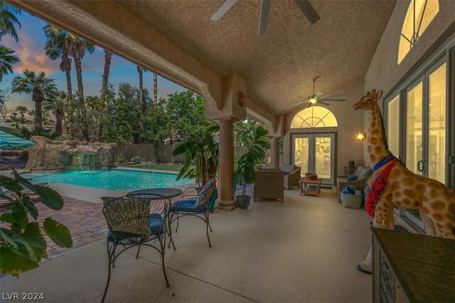 pool at dusk featuring ceiling fan, pool water feature, and a patio