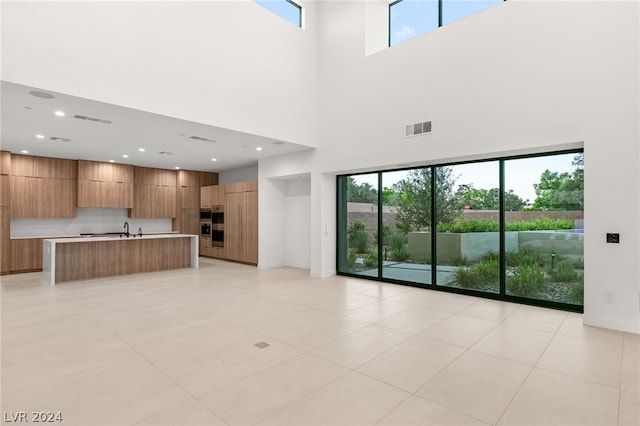 unfurnished living room with light tile patterned flooring, a towering ceiling, sink, and a wealth of natural light