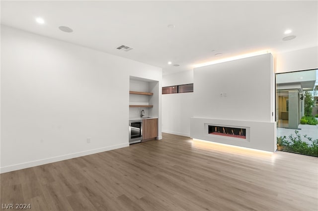 unfurnished living room featuring built in shelves, sink, beverage cooler, wood-type flooring, and a fireplace