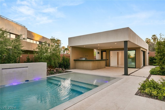 view of swimming pool with pool water feature, an outdoor kitchen, and a patio