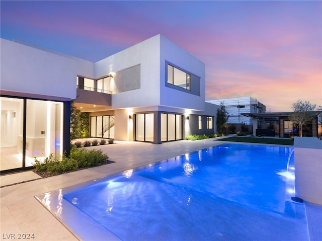 pool at dusk with pool water feature and a patio area