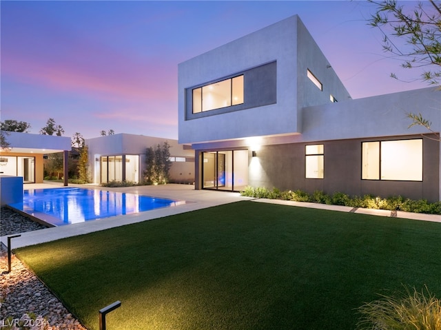 pool at dusk featuring a yard, an outbuilding, and a patio