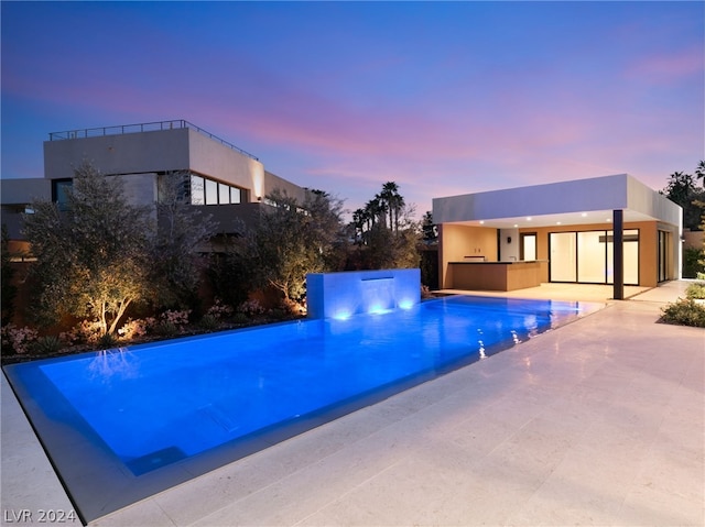 pool at dusk with a patio and area for grilling