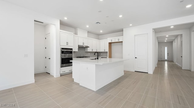 kitchen with light tile patterned floors, sink, a center island with sink, white cabinetry, and decorative backsplash