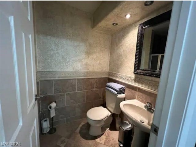 bathroom featuring toilet, sink, and tile walls