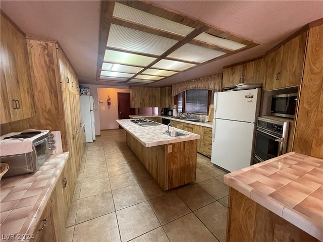 kitchen featuring appliances with stainless steel finishes, light tile floors, sink, an island with sink, and tile counters