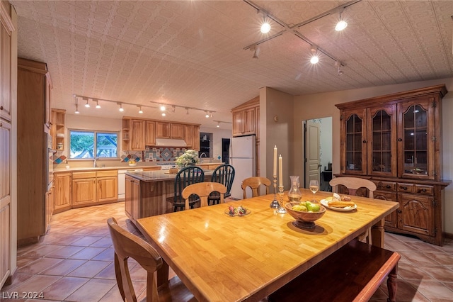 dining space featuring sink, light tile patterned floors, lofted ceiling, and track lighting