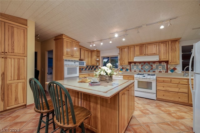 kitchen featuring white appliances, a kitchen bar, backsplash, a center island, and track lighting