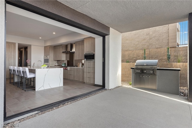 kitchen featuring wall chimney range hood, a kitchen breakfast bar, an island with sink, a textured ceiling, and tile walls