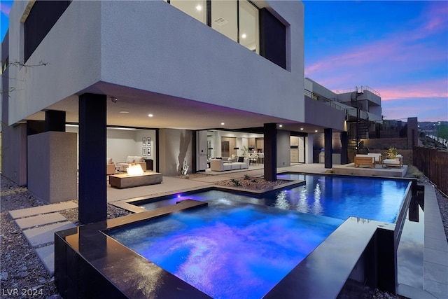 pool at dusk with an in ground hot tub, an outdoor living space with a fire pit, and a patio area