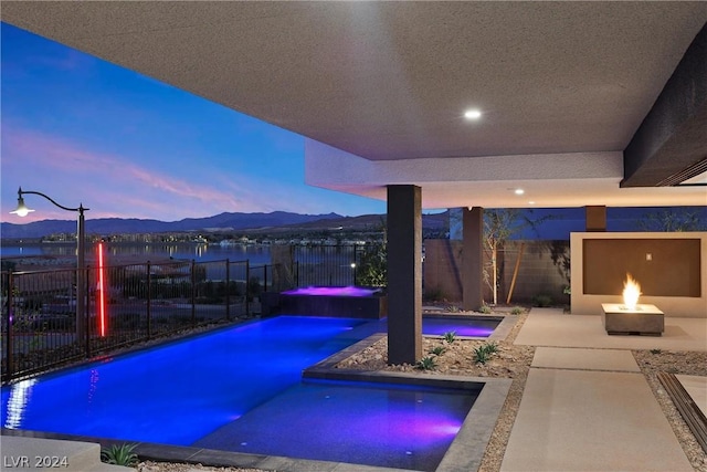 pool at dusk featuring an in ground hot tub, a mountain view, and a fire pit