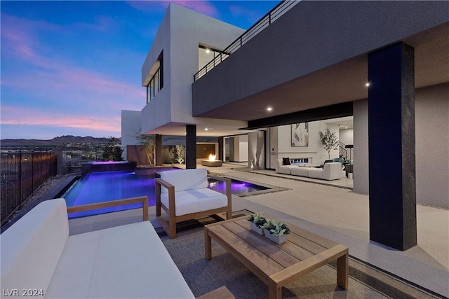 pool at dusk featuring an in ground hot tub, an outdoor living space, and a patio