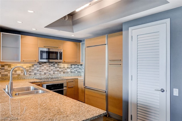 kitchen featuring appliances with stainless steel finishes, tasteful backsplash, light stone countertops, light brown cabinets, and sink