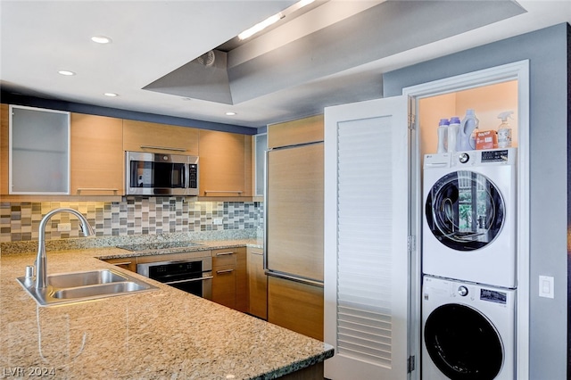 kitchen with appliances with stainless steel finishes, stacked washer / dryer, sink, and tasteful backsplash