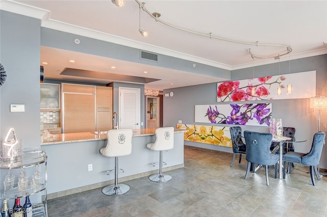 interior space with ornamental molding, kitchen peninsula, backsplash, a breakfast bar, and light stone countertops