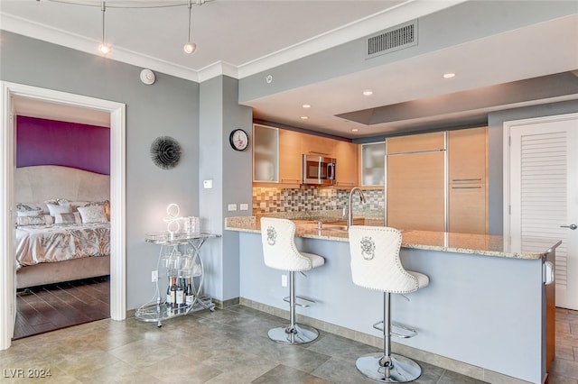 kitchen with light stone counters, ornamental molding, a breakfast bar area, and kitchen peninsula