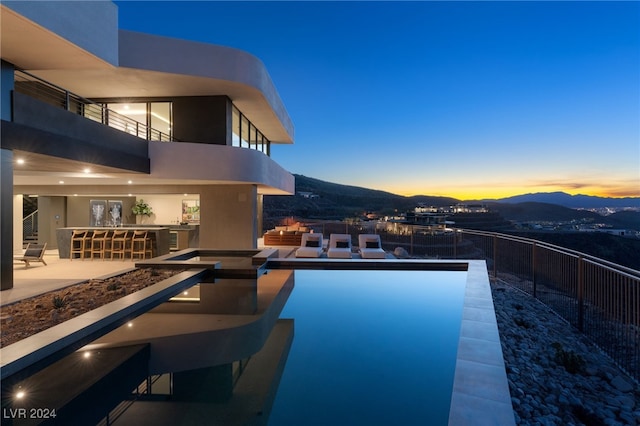 pool at dusk featuring a patio, a mountain view, and a bar