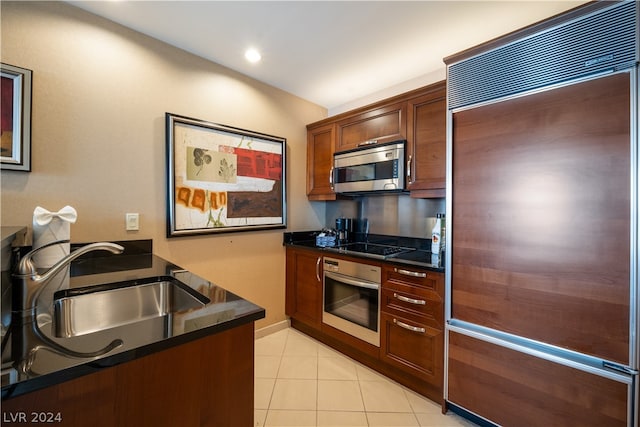 kitchen featuring sink, light tile patterned flooring, dark stone counters, and stainless steel appliances