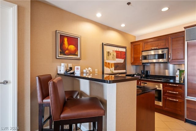 kitchen featuring kitchen peninsula, appliances with stainless steel finishes, light tile patterned flooring, and a breakfast bar