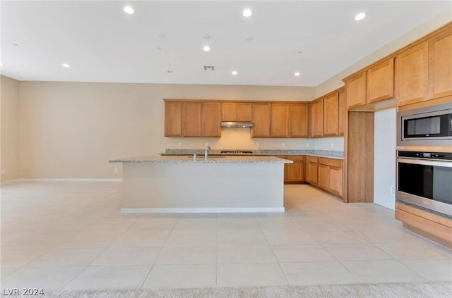 kitchen featuring a center island with sink, light tile patterned floors, light stone countertops, and appliances with stainless steel finishes