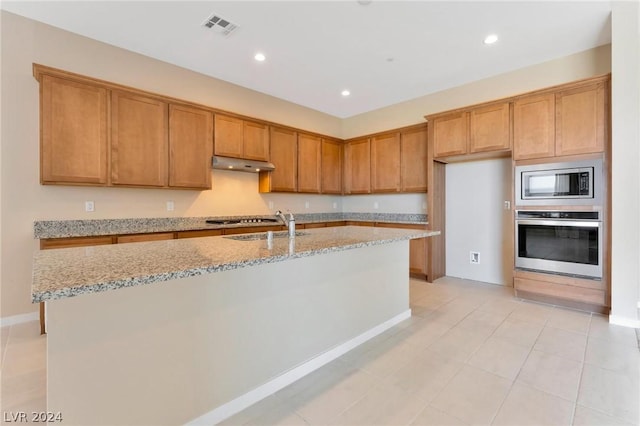 kitchen featuring a center island with sink, sink, light tile patterned floors, light stone countertops, and appliances with stainless steel finishes