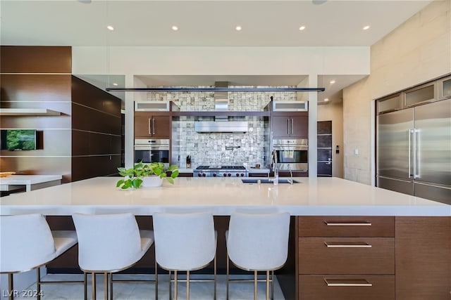 kitchen with stainless steel appliances, backsplash, sink, a large island, and a breakfast bar