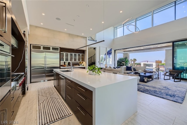 kitchen featuring a sink, dark brown cabinetry, modern cabinets, stainless steel built in refrigerator, and a large island with sink