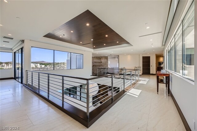 corridor featuring a raised ceiling and light tile floors