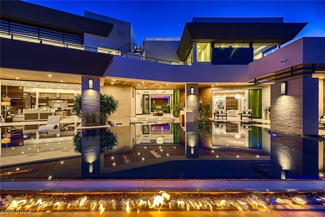 back of house at night featuring a balcony and stucco siding