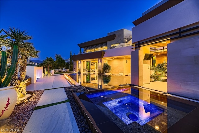 pool at twilight featuring a patio area and an in ground hot tub