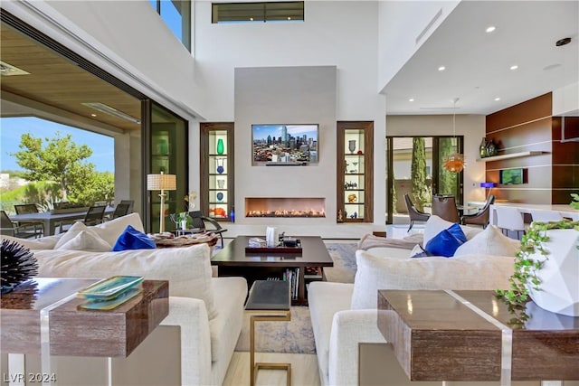 living room with a lit fireplace, wood finished floors, a towering ceiling, and recessed lighting