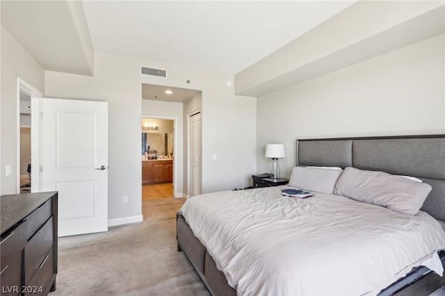 bedroom featuring connected bathroom, light colored carpet, and a closet