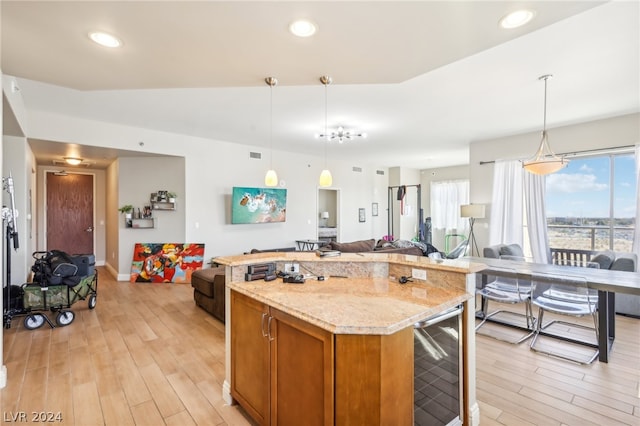 kitchen featuring pendant lighting, a center island, light stone counters, beverage cooler, and light wood-type flooring