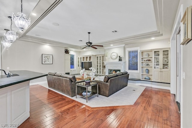 living room with dark hardwood / wood-style floors, built in features, a raised ceiling, and ceiling fan with notable chandelier